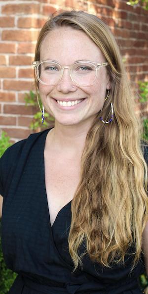 Jessie Carver portrait with long blonde hair, glasses in a black shirt